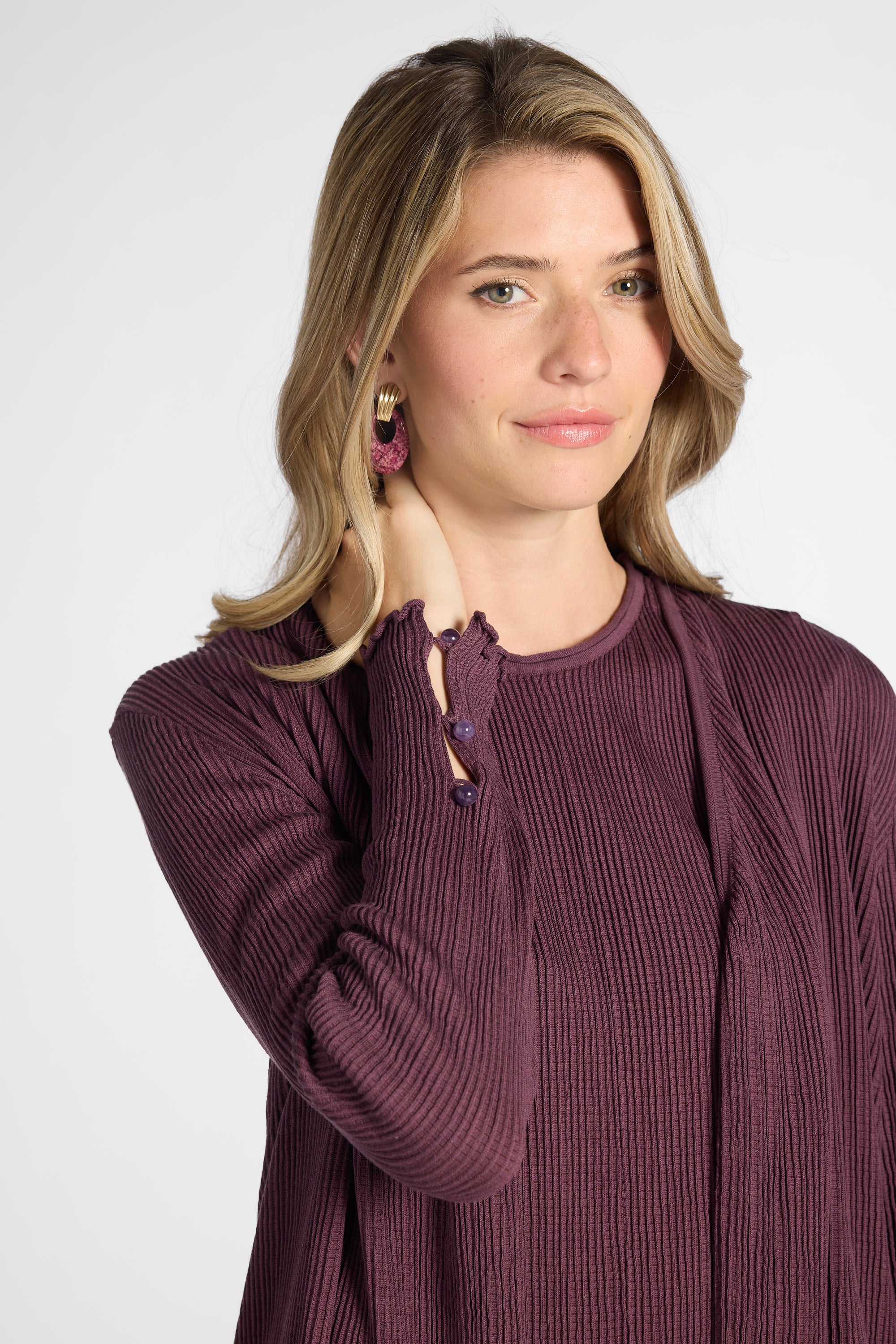 Woman modeling a pleated purple cardigan with purple quartz buttons on the sleeve against a white backdrop
