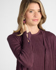 Woman modeling a pleated purple cardigan with purple quartz buttons on the sleeve against a white backdrop
