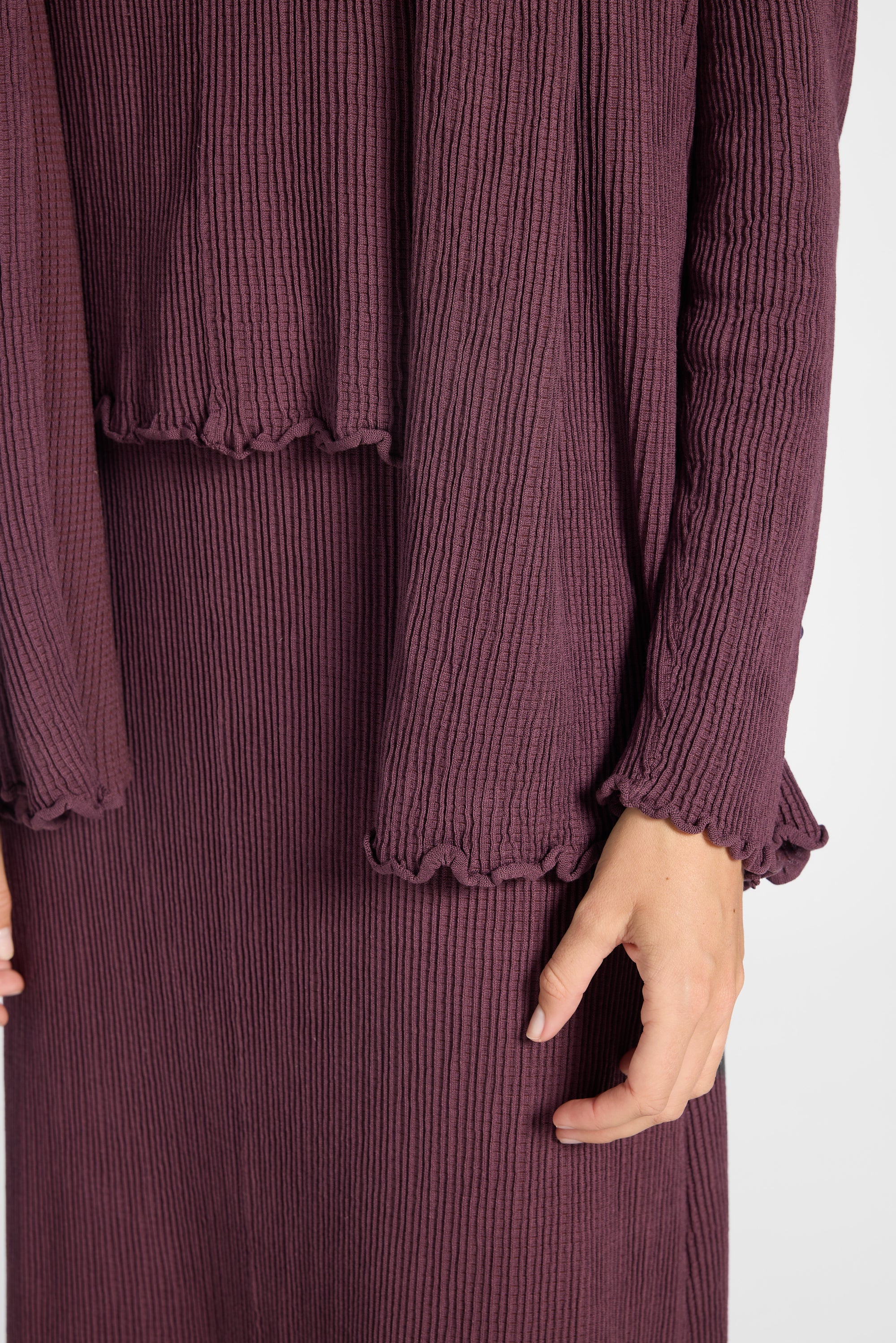 Close up image  of a purple silk pleated cardigan, skirt, and shell on a white backdrop