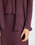 Close up image  of a purple silk pleated cardigan, skirt, and shell on a white backdrop
