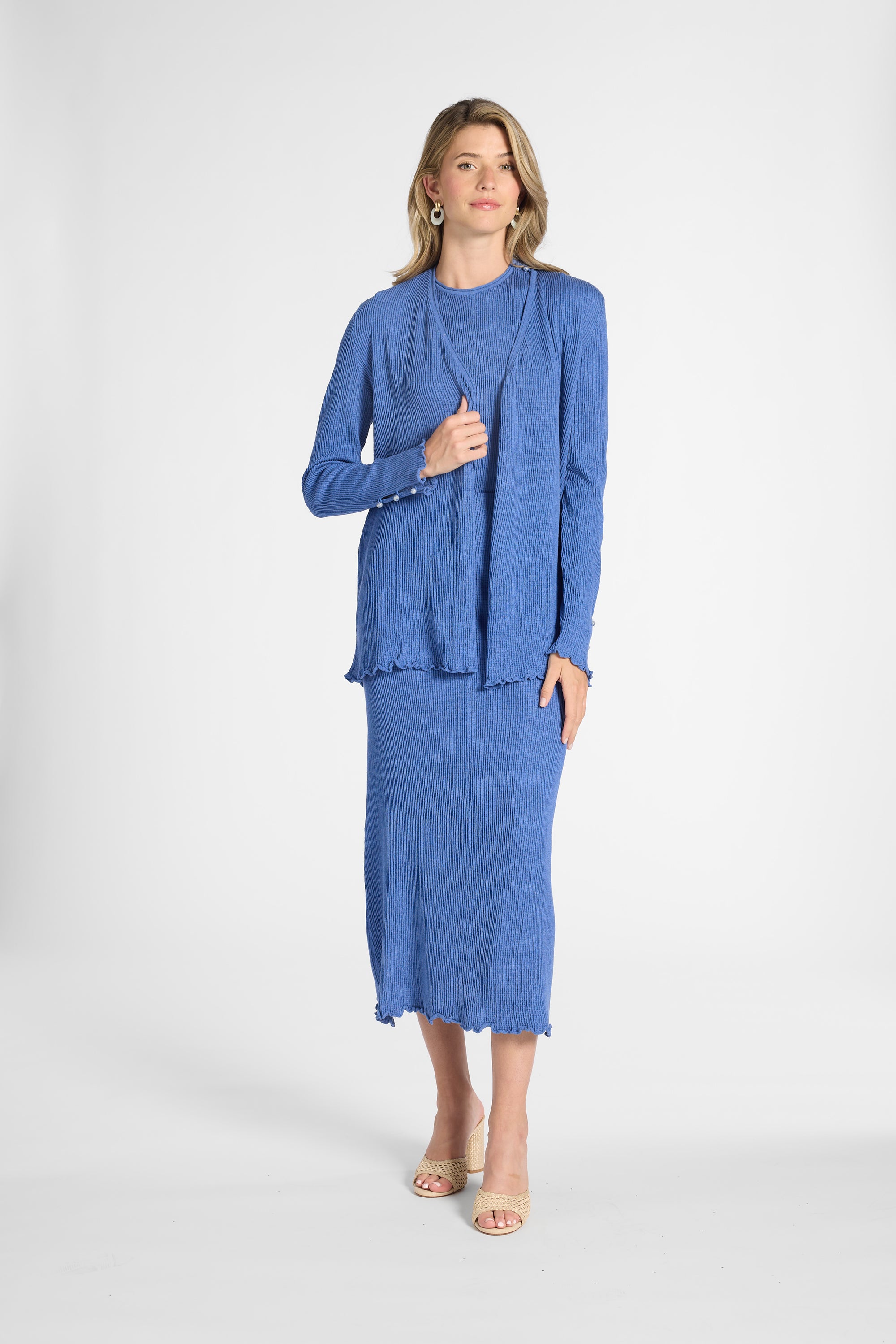 Woman modeling a blue pleated cardigan with gemstone buttons on the sleeve on a white backdrop