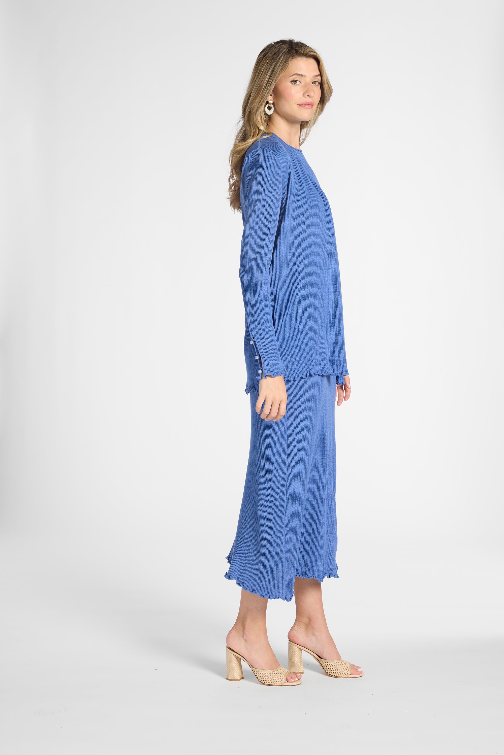 Woman modeling a pleated blue cardigan with gemstones on a white backdrop