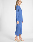 Woman modeling a pleated blue cardigan with gemstones on a white backdrop