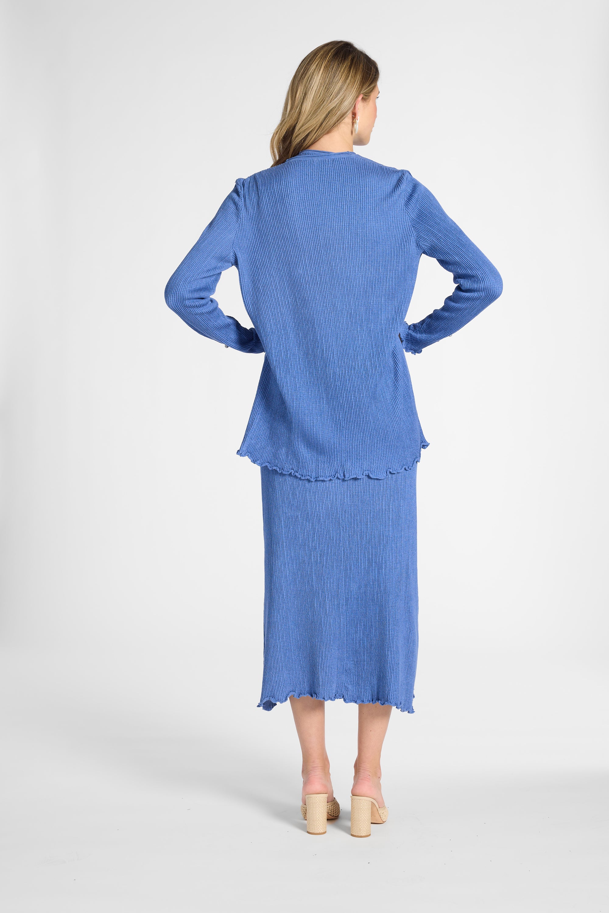 A woman modeling a pleated blue cardigan and matching skirt on a white backdrop