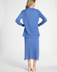 A woman modeling a pleated blue cardigan and matching skirt on a white backdrop