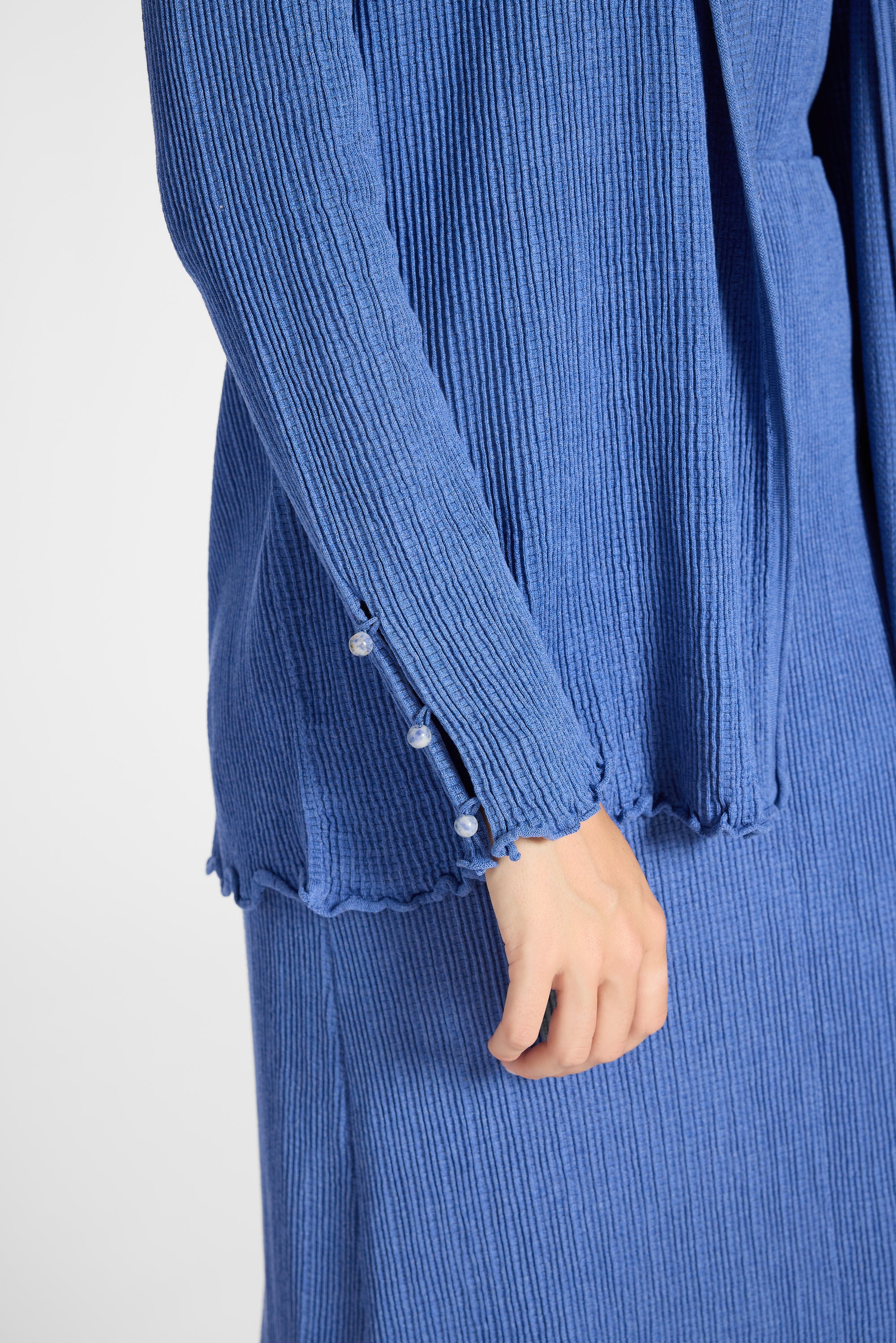 Close up image of a pleated blue cardigan with gemstone buttons on the sleeve
