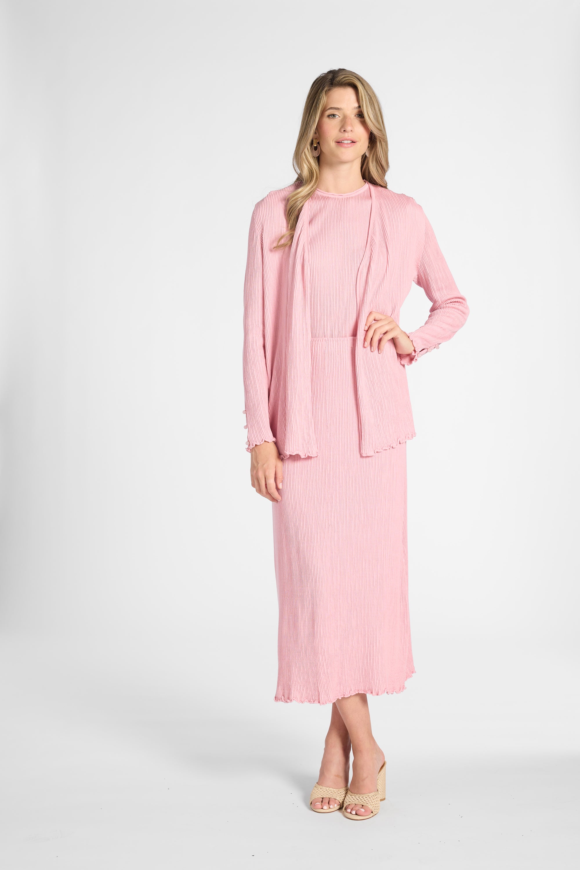 Woman dressed in a silk pleated pink cardigan and skirt on a white backdrop