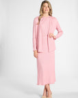 Woman dressed in a silk pleated pink cardigan and skirt on a white backdrop
