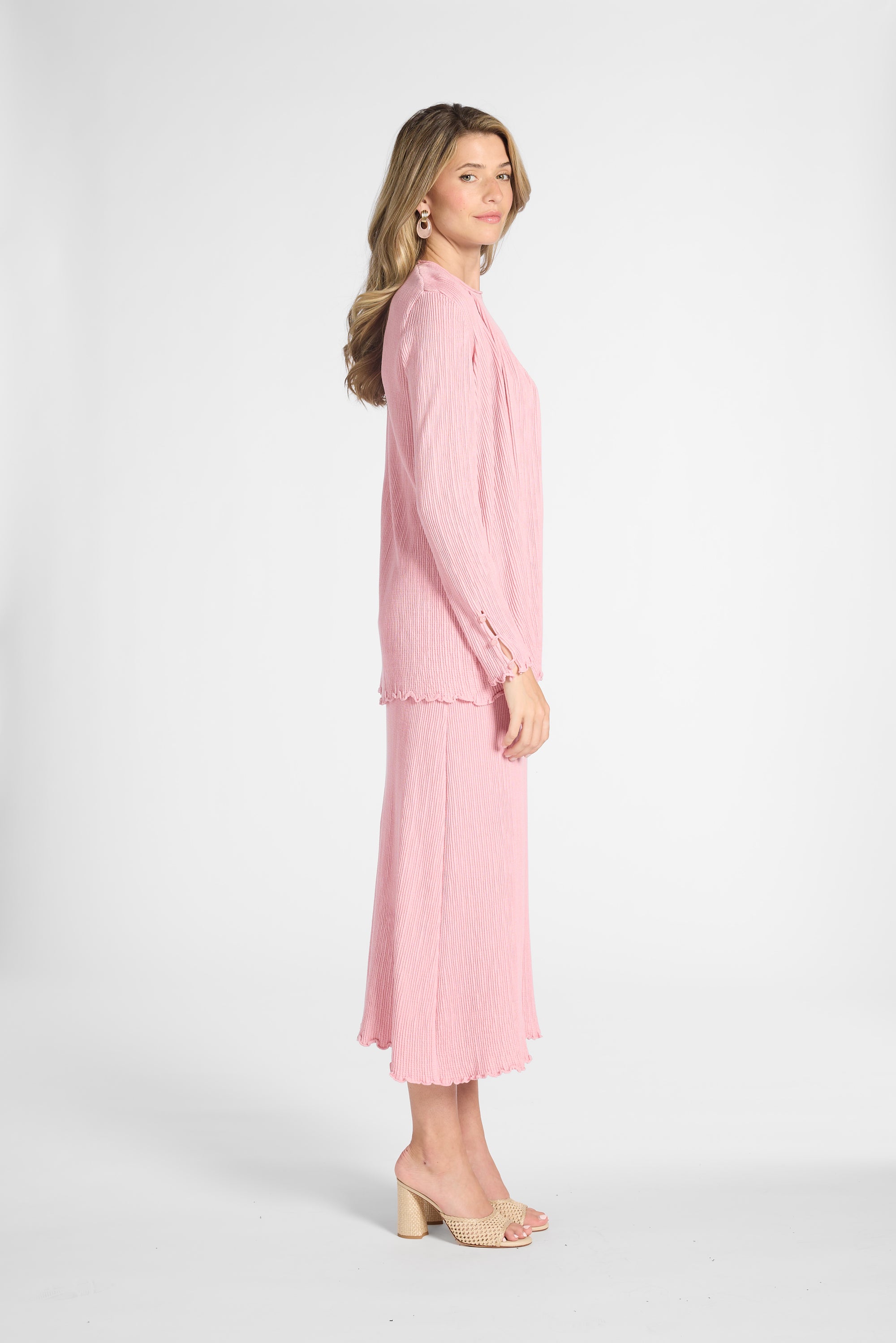 Woman modeling a silk pink cardigan and the matching skirt with nude heels on a white backdrop