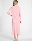 Woman standing to the back modeling a pink cardigan and the matching pleated skirt on a white backdrop