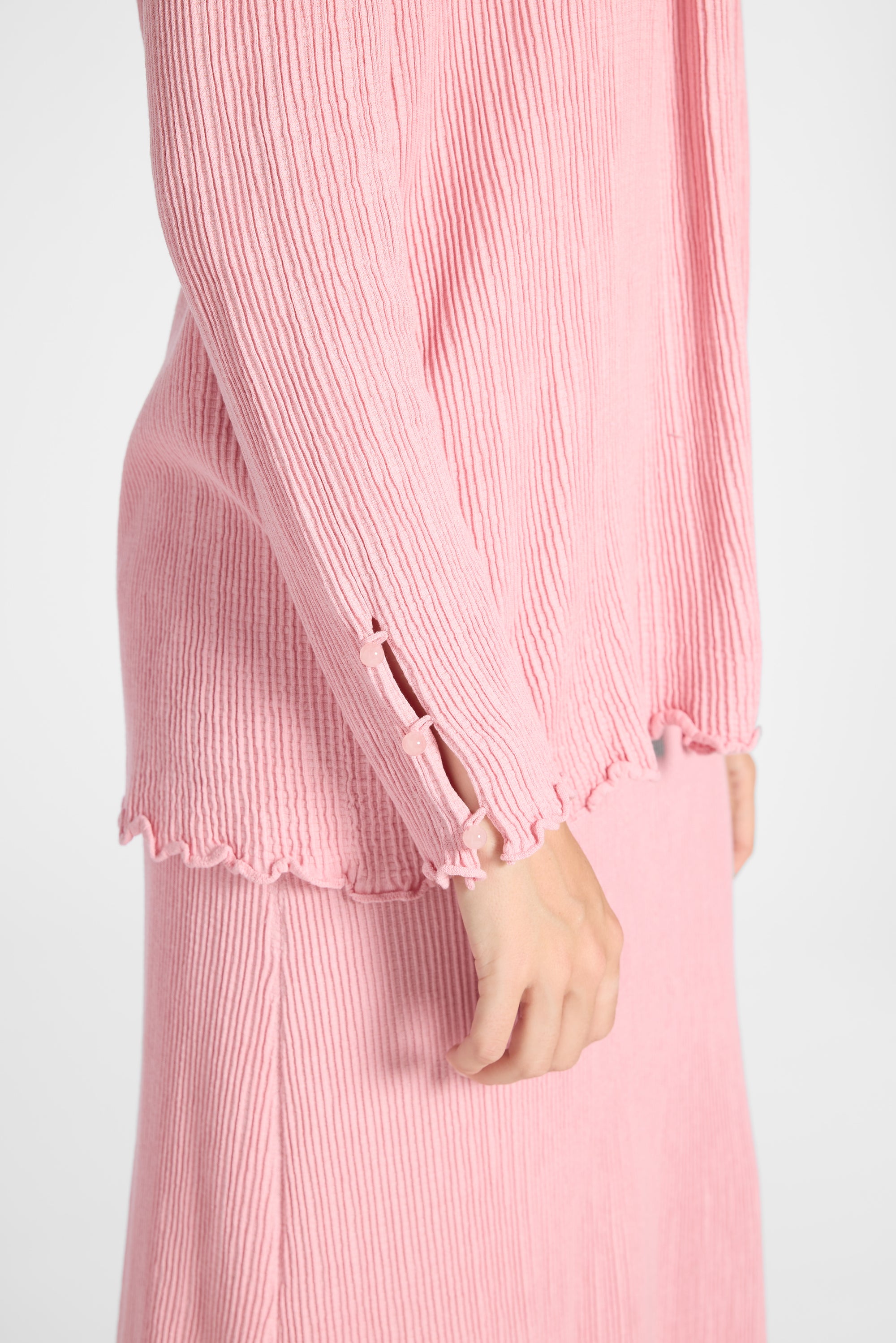 Close up of a pleated silk pink cardigan with pink quartz gemstones along the sleeve on a white backdrop