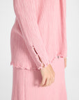 Close up of a pleated silk pink cardigan with pink quartz gemstones along the sleeve on a white backdrop