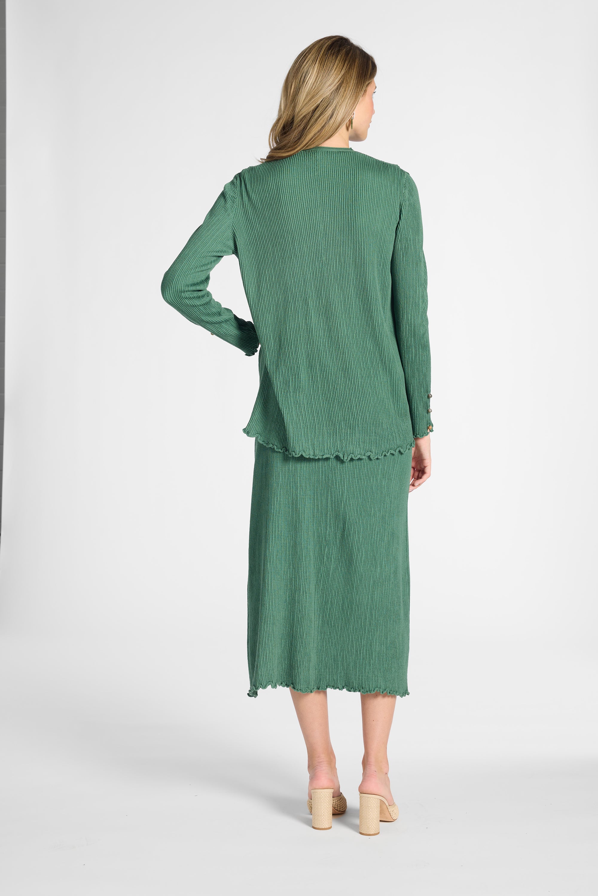 Woman modeling a pleated green cardigan with gemstones with the matching pleated skirt on a white background