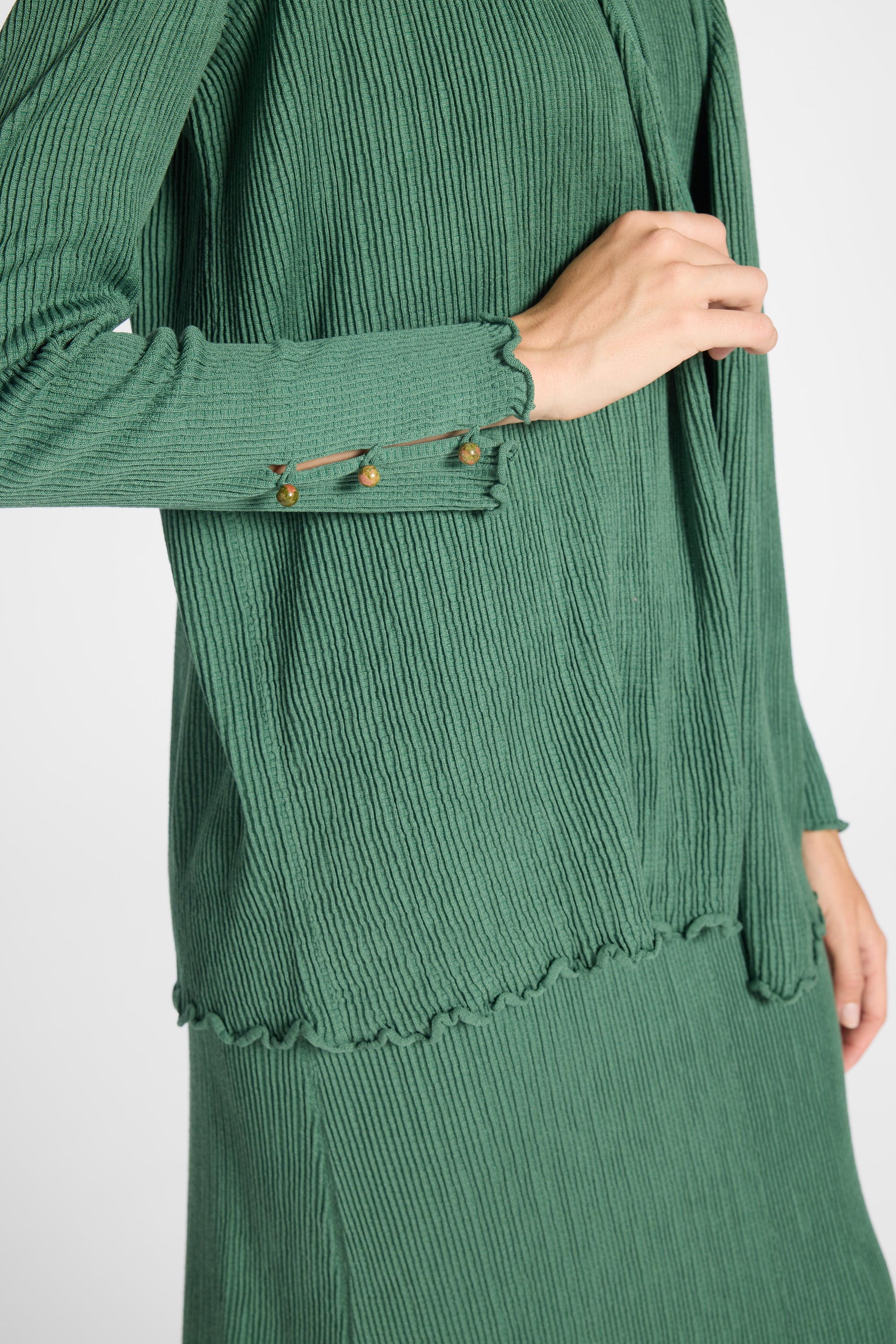 Close up of a pleated green silk cardigan with gemstones on a white backdrop
