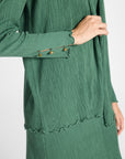 Close up of a pleated green silk cardigan with gemstones on a white backdrop
