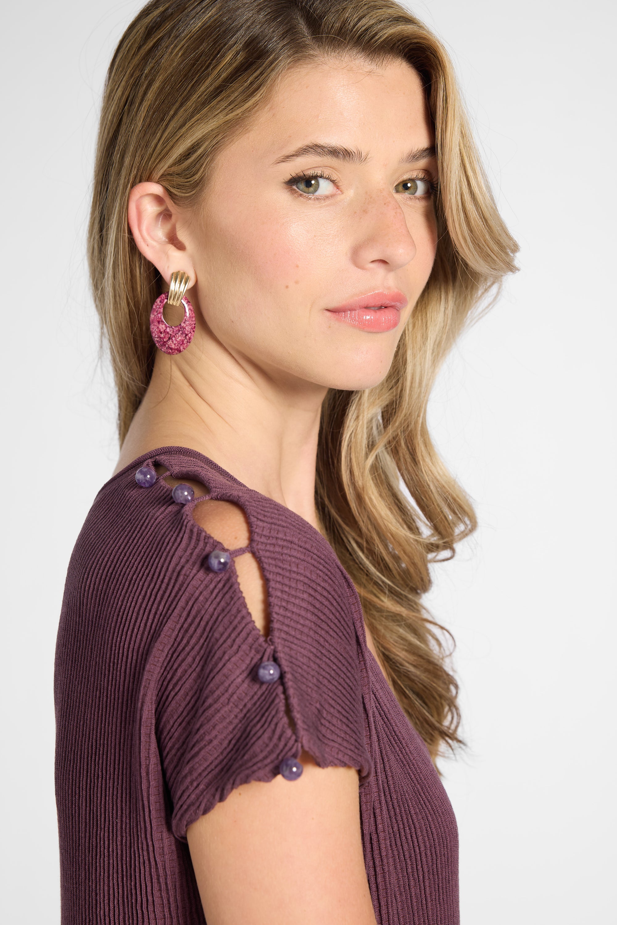 Close up of the shoulder of a silk purple pleated dress with purple quartz buttons on the shoulder