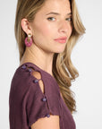 Close up of the shoulder of a silk purple pleated dress with purple quartz buttons on the shoulder