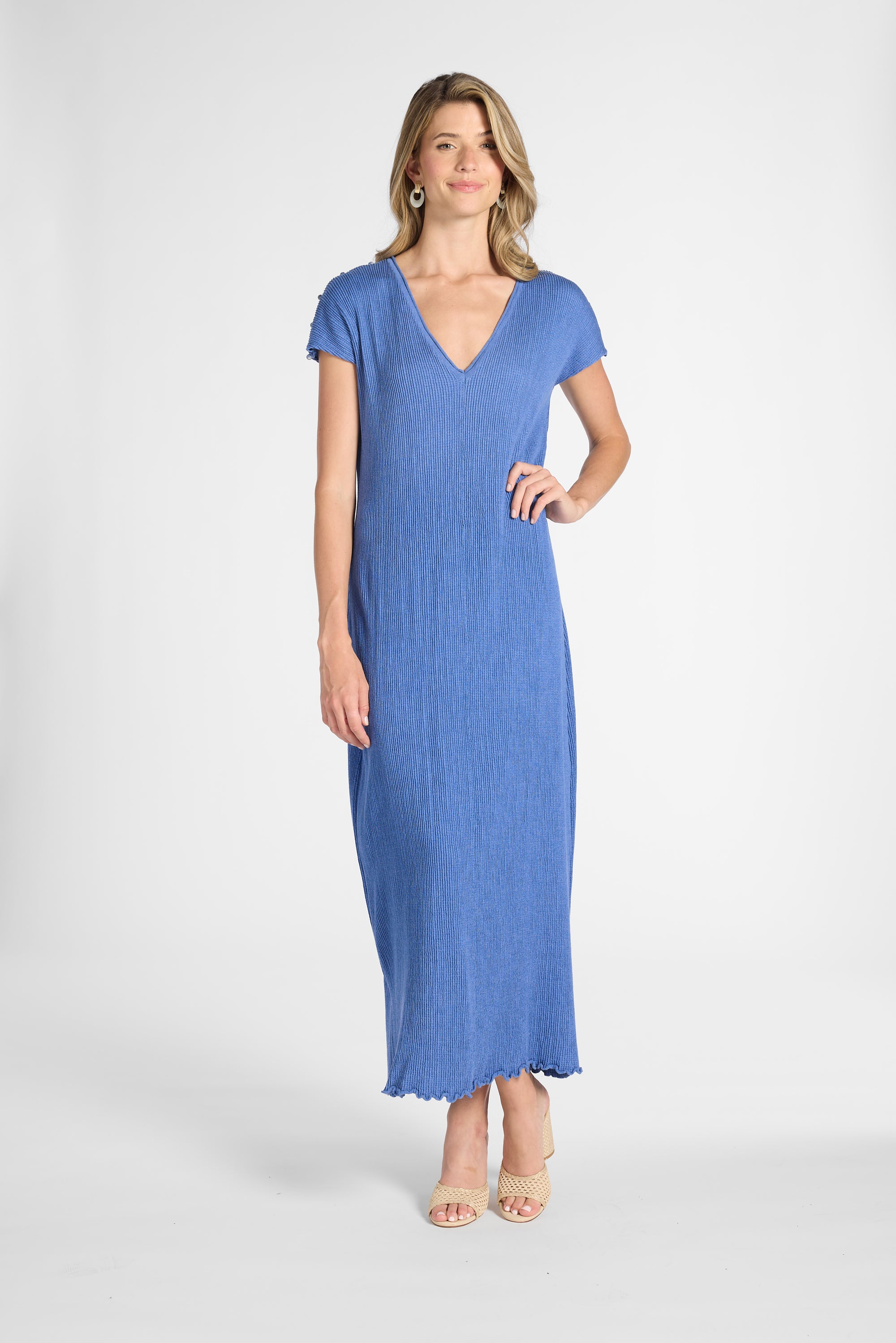 A woman modeling a blue pleated silk dress with nude heels on a white background