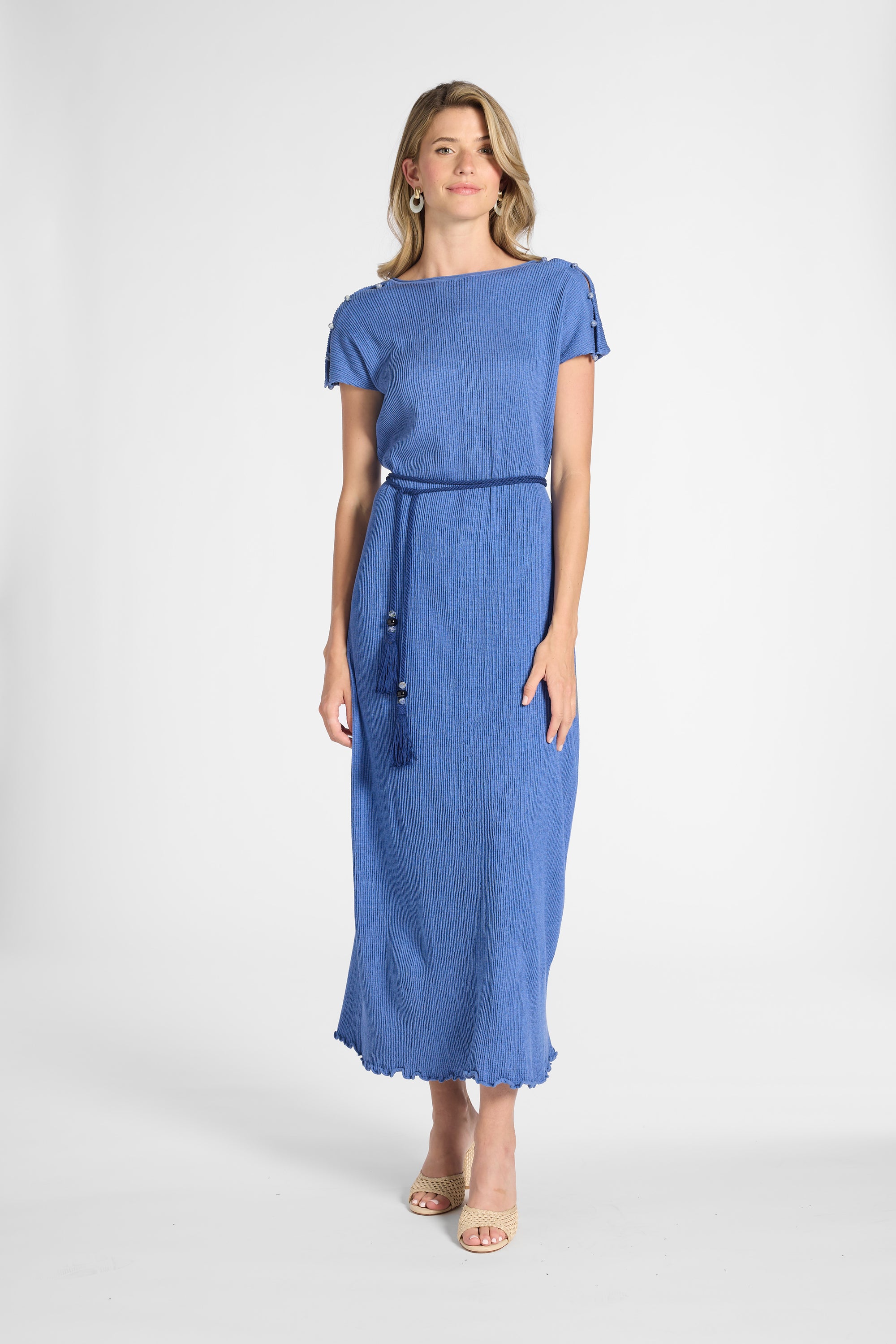 A woman modeling a blue pleated dress with a tassel around the waist on a white backdrop