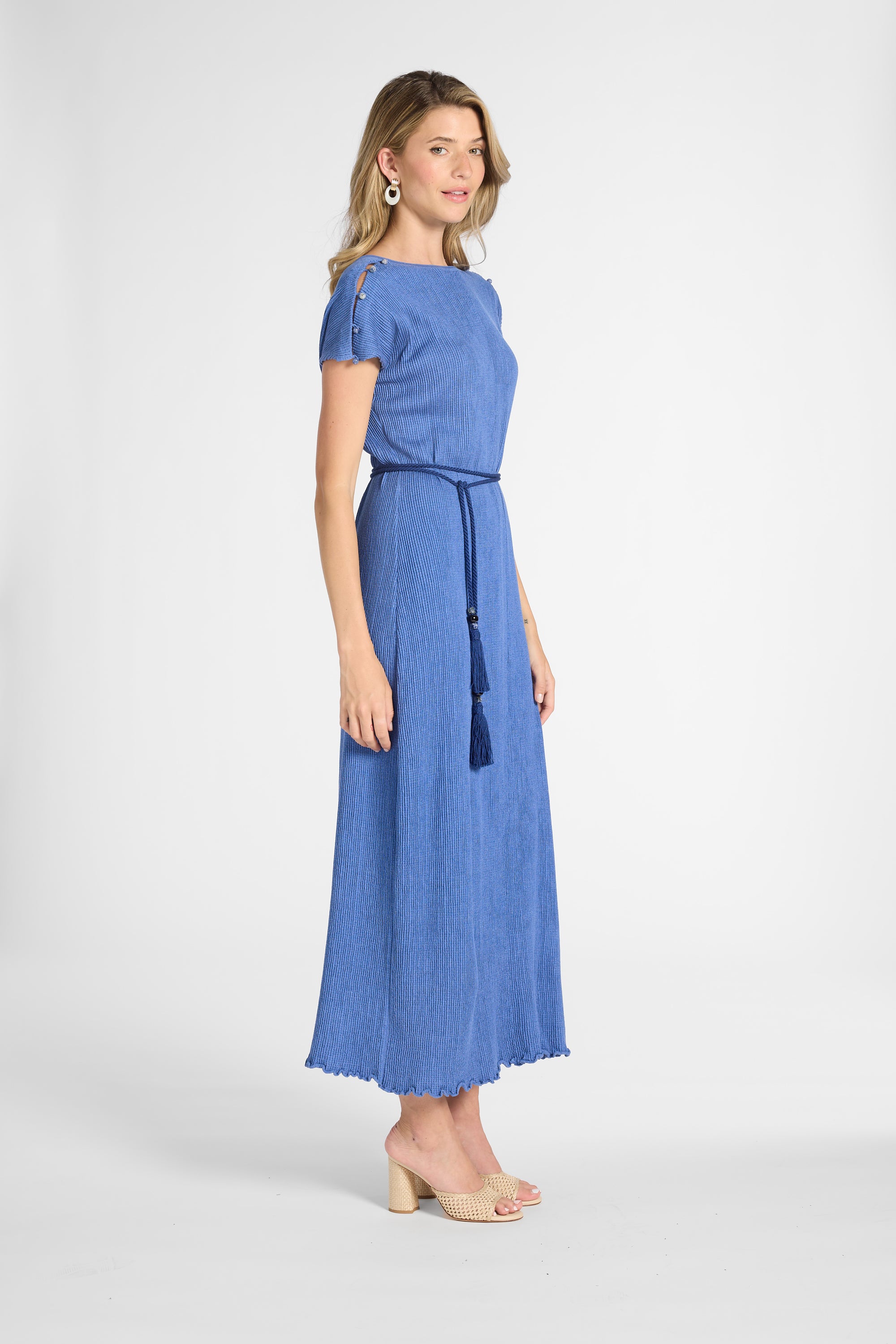 A woman modeling a blue short-sleeve maxi dress with a matching tie belt and tassel, shown in profile against a light gray studio background.