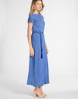 A woman modeling a blue short-sleeve maxi dress with a matching tie belt and tassel, shown in profile against a light gray studio background.