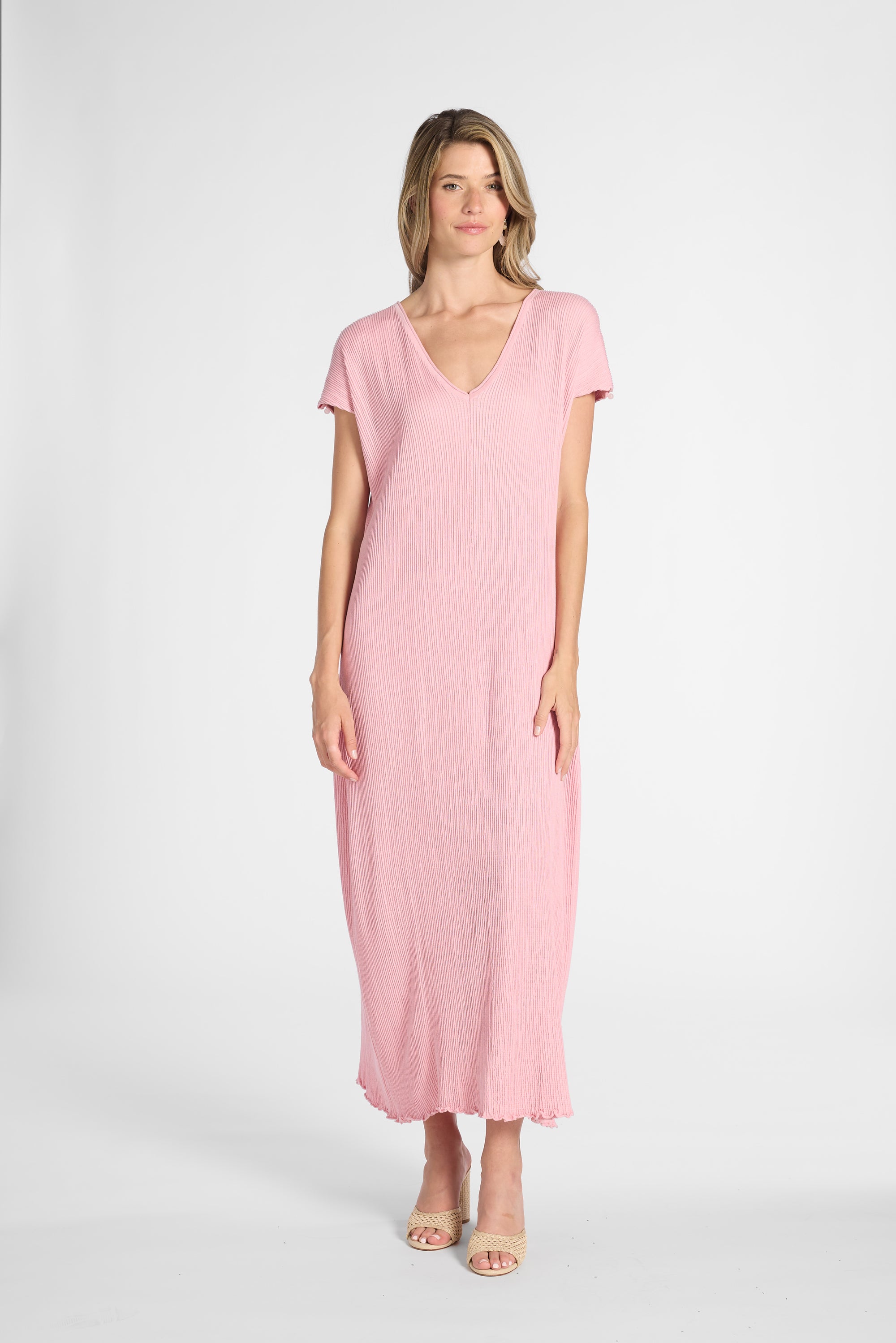 A woman modeling a light pink short-sleeve maxi dress with a V-neckline, photographed against a plain light gray studio background.