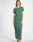A woman modeling a green short-sleeve maxi dress with decorative tassel details on the waist and sleeve edges, photographed against a plain light gray studio background.