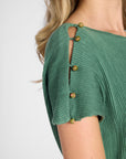 Close up of the shoulder of the pleated green dress with gemstone buttons on the shoulder