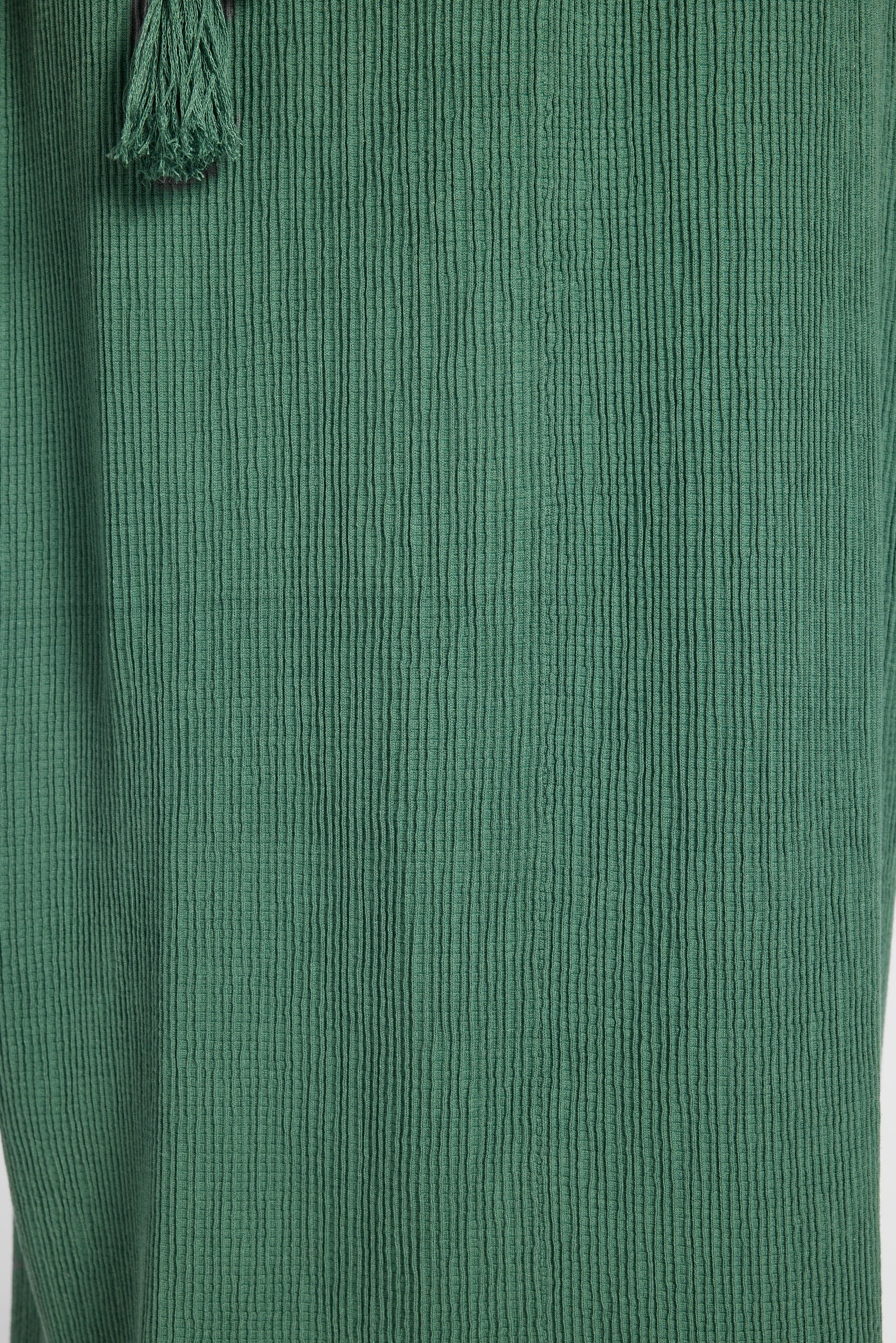 Close-up of a green pleated fabric with a small tassel detail at the top left.