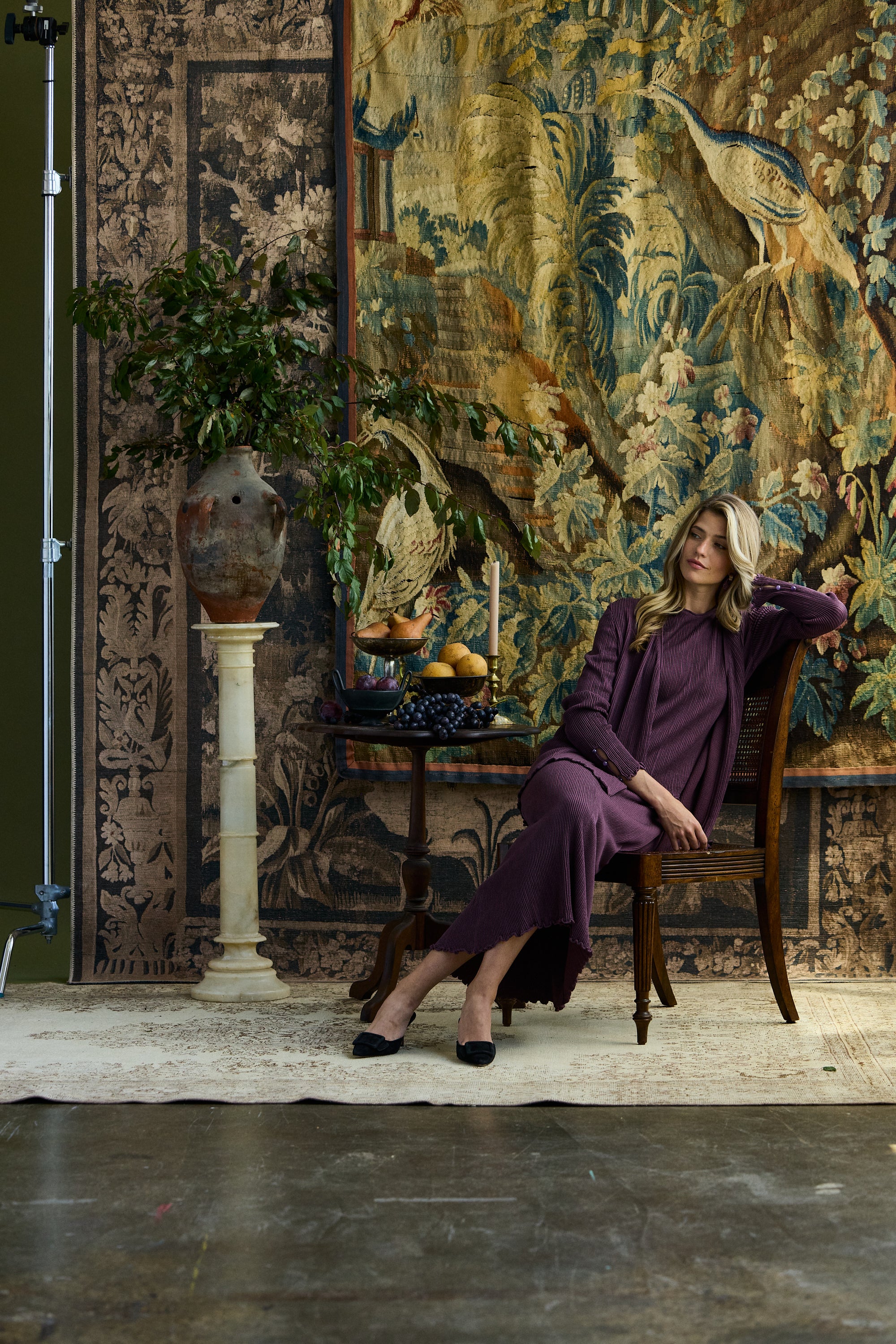 Woman sitting against rugs wearing a pleated purple silk cardigan with gemstone buttons