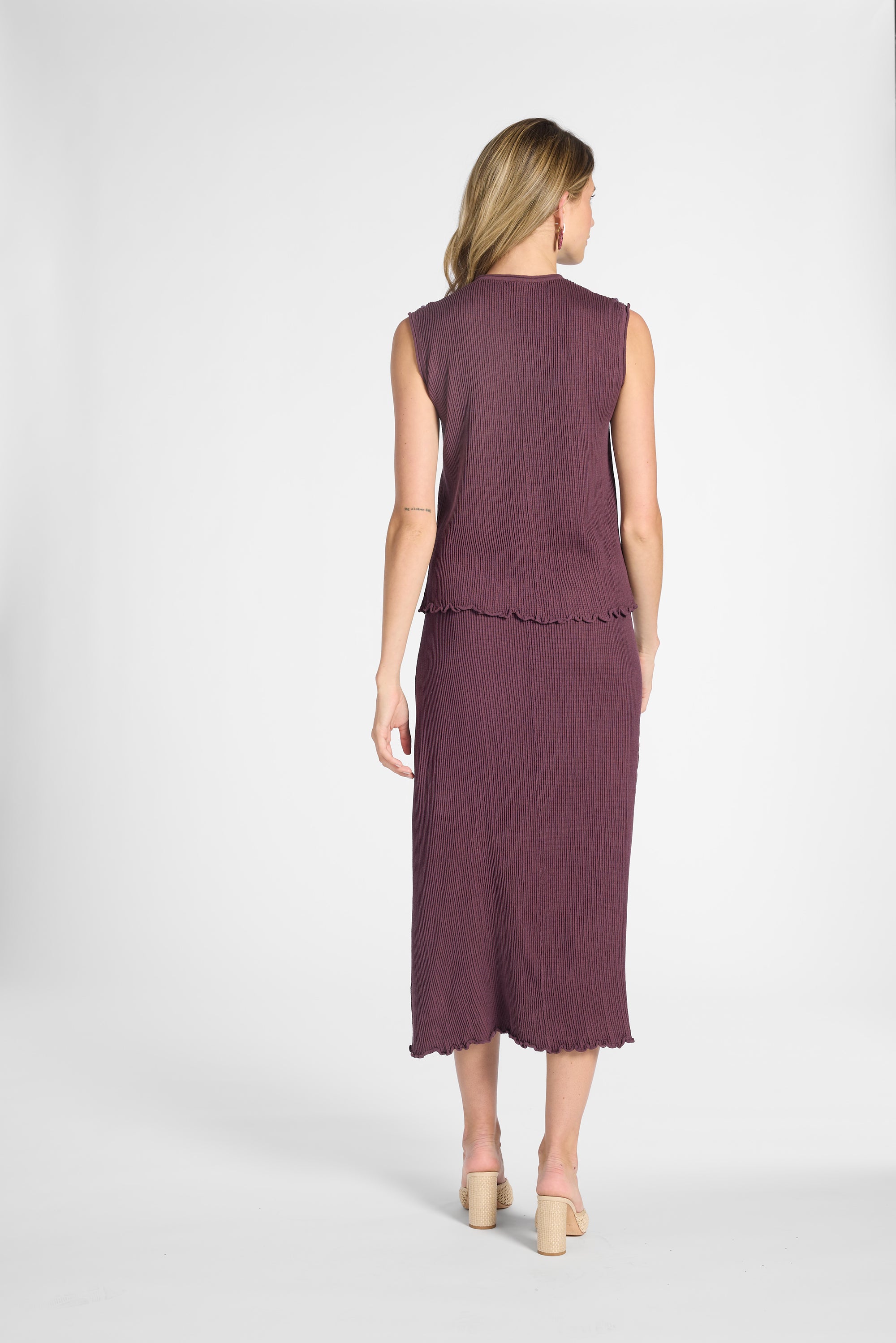 Woman wearing a pleated purple silk tank top and matching silk skirt on a white background