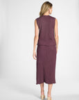 Woman wearing a pleated purple silk tank top and matching silk skirt on a white background