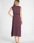 Woman standing with her back facing the camera wearing a pleated purple skirt on a white backdrop