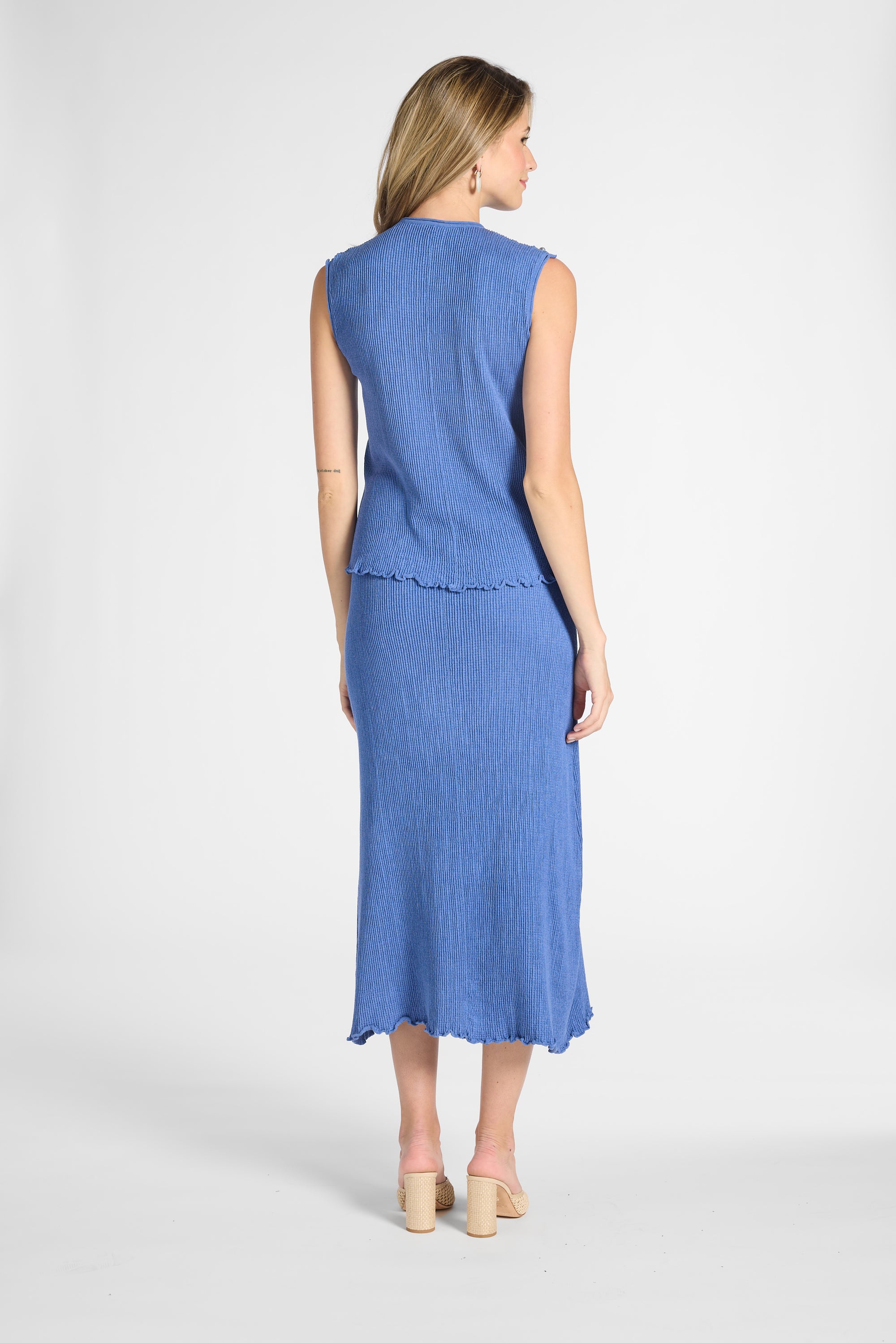 Woman standing towards the back modeling a pleated blue skirt and shell on a white backdrop