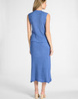 Woman standing towards the back modeling a pleated blue skirt and shell on a white backdrop