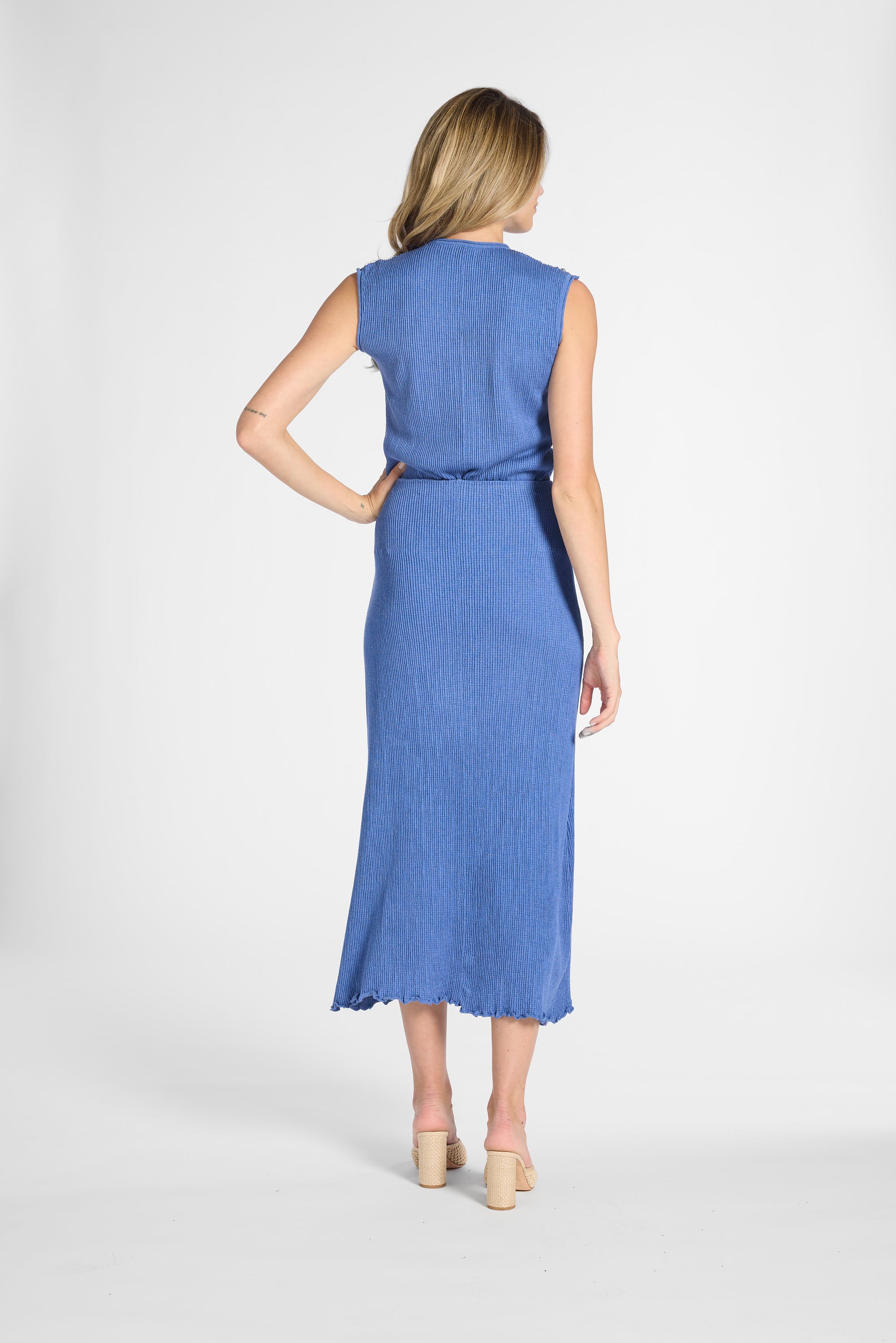 A woman modeling a pleated shell and skirt from the back, standing against a light gray studio background.