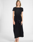 Woman modeling a pleated black silk dress with a tassel around the waist on a white backdrop