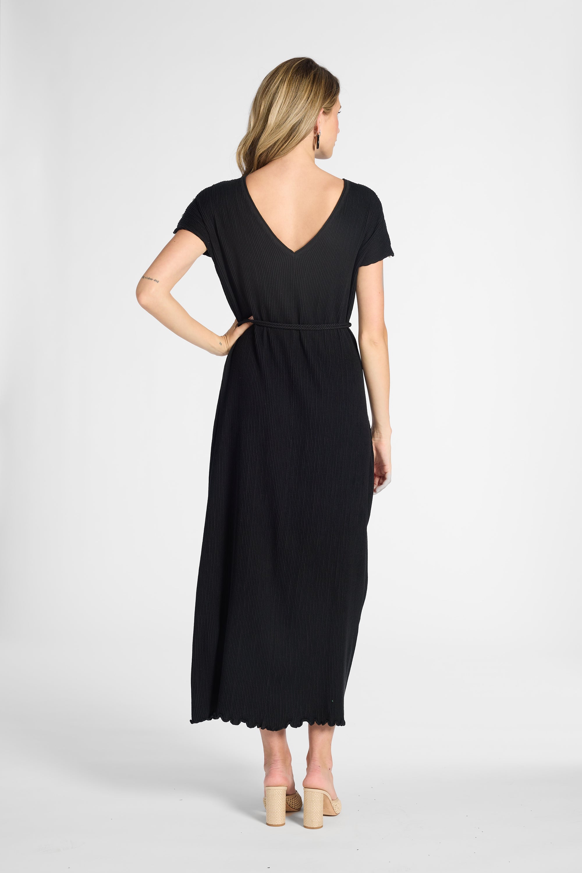A woman wearing a pleated onyx dress on a white background with nude heels
