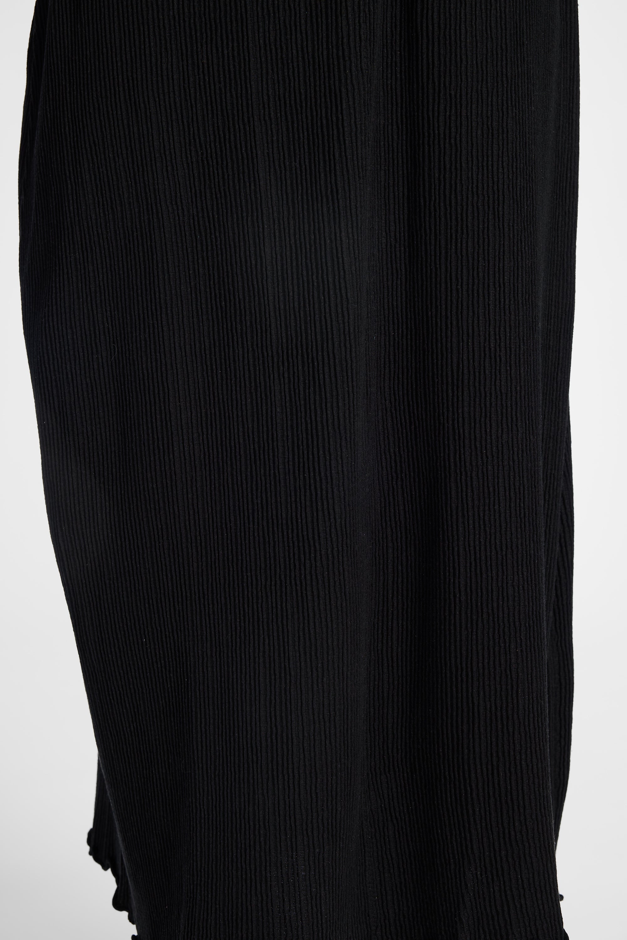 Close-up of a black pleated dress with vertical ribbed texture against a plain light background.