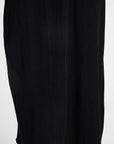 Close-up of a black pleated dress with vertical ribbed texture against a plain light background.
