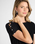 Image of the shoulder of a black silk pleated dress with white gemstones on a white background