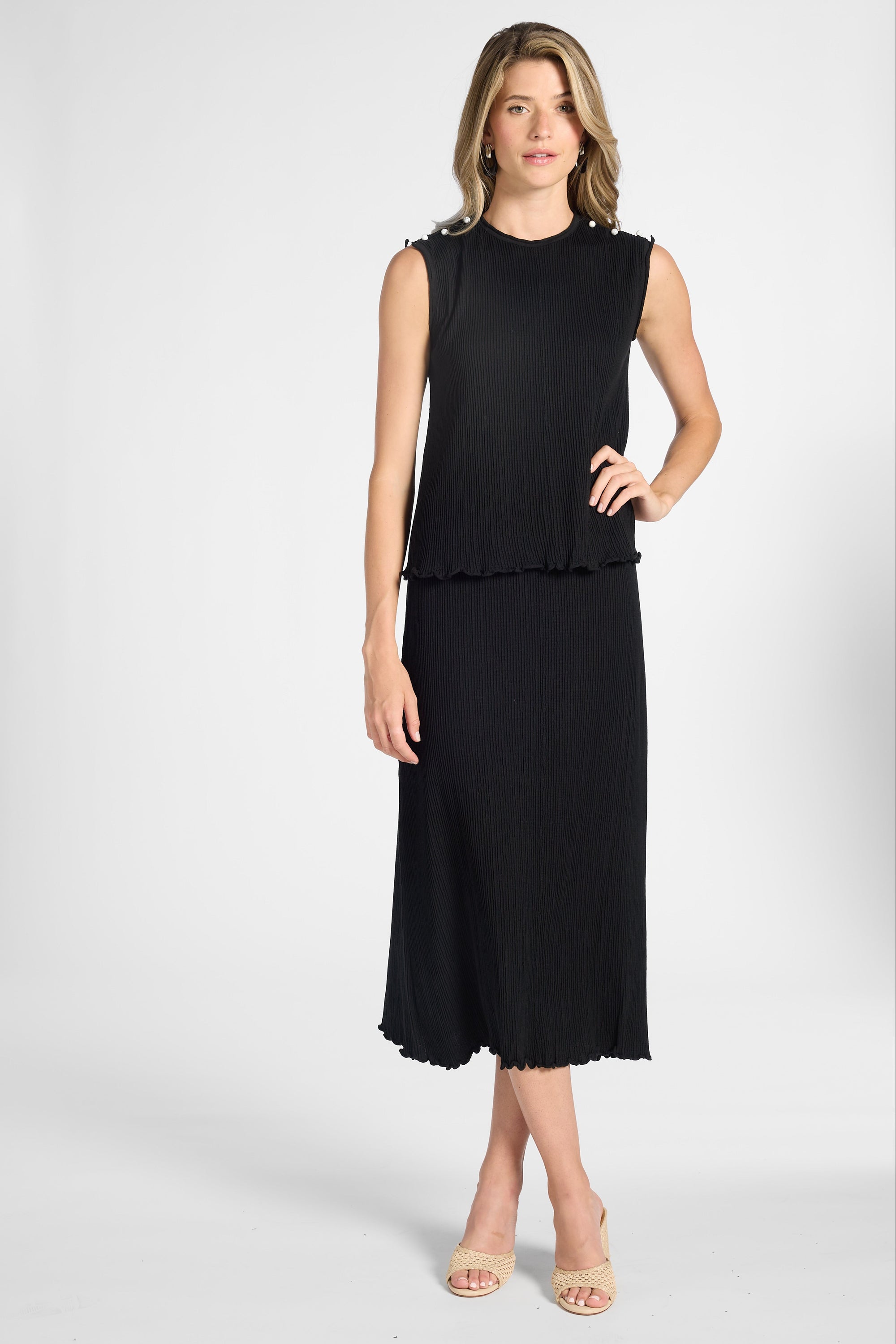 A woman modeling a pleated silk shell with the matching black skirt on a white backdrop