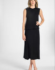 A woman modeling a pleated silk shell with the matching black skirt on a white backdrop