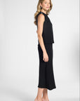 A woman modeling a sleeveless black midi dress with a ruffled peplum-style waist and a flared skirt, photographed against a white studio background.