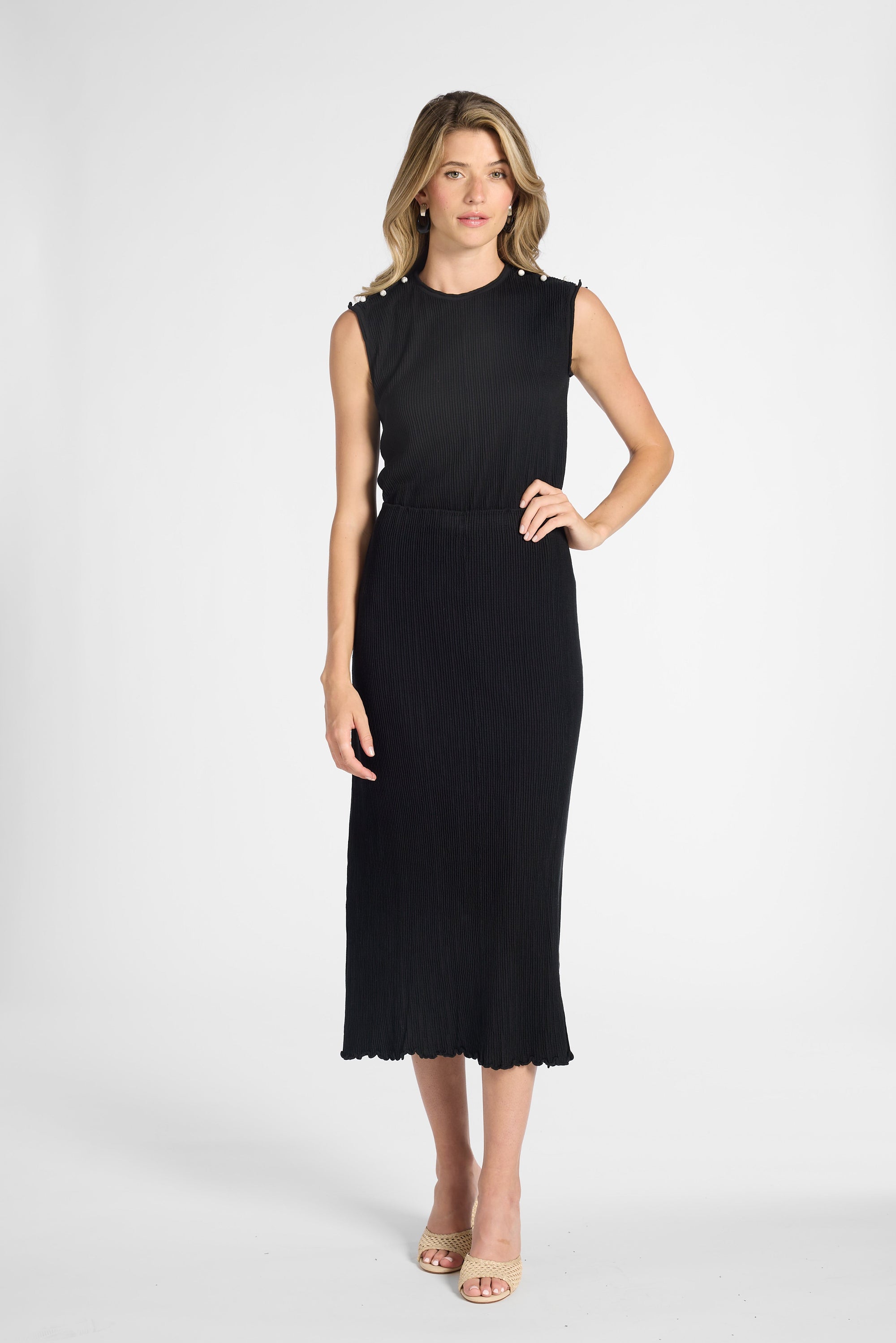 Woman modeling a pleated black shell with the matching skirt on a white backdrop