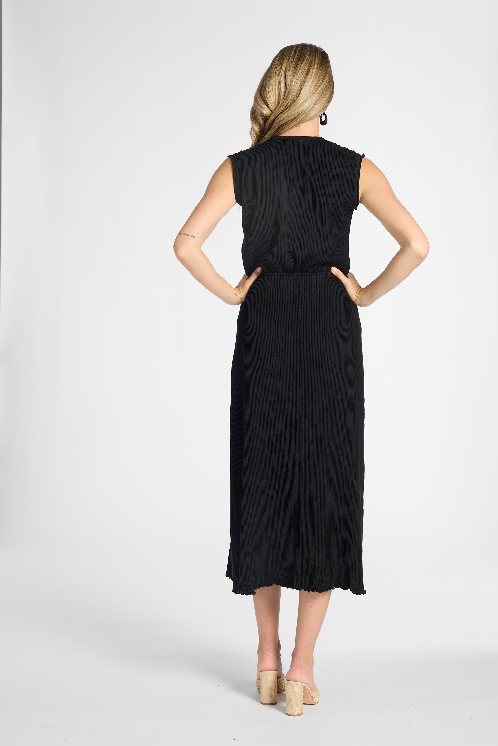 A woman shown from the back wearing a black skirt, standing against a light gray studio background.