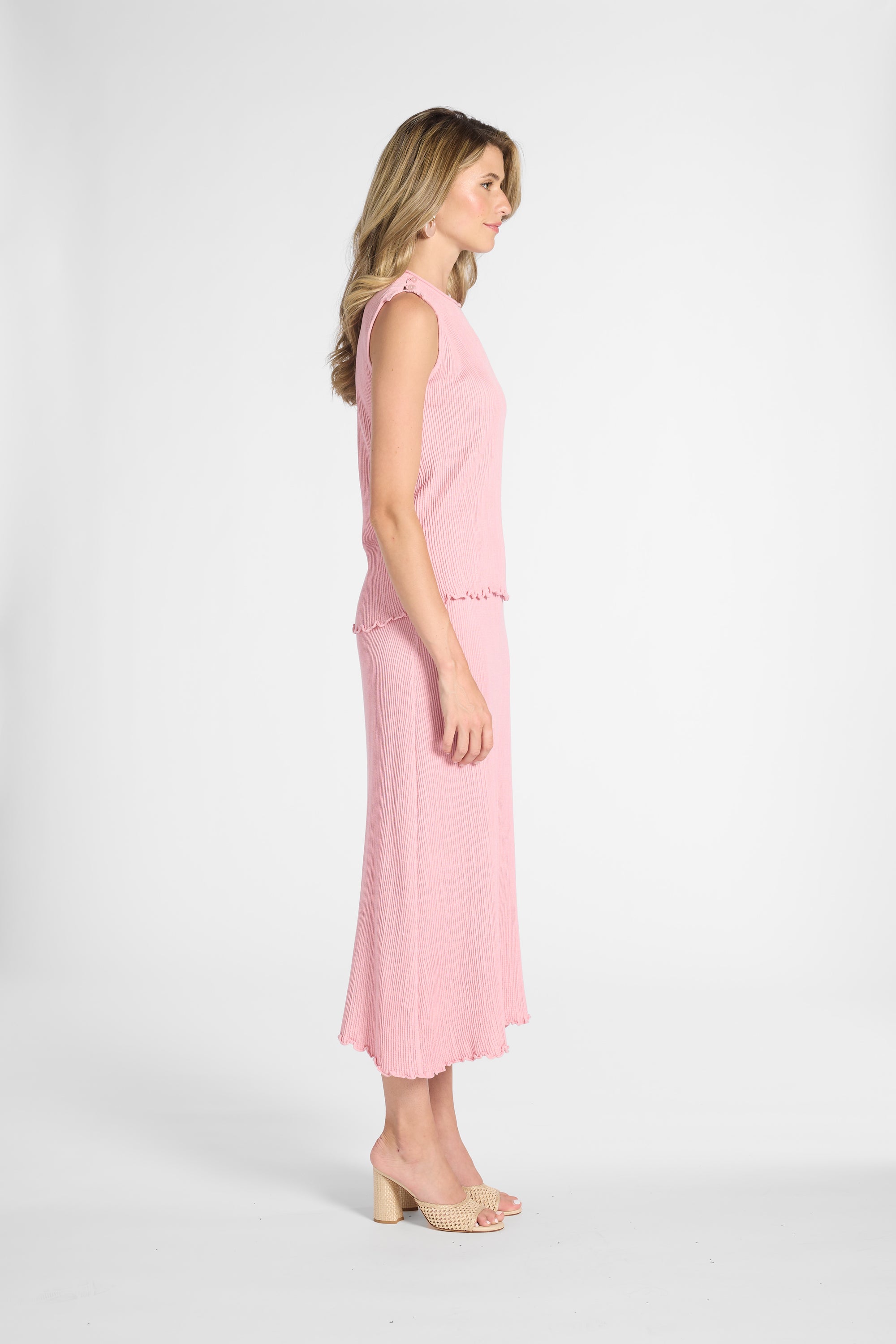 Woman standing to the side modeling a light pink pleated shell and skirt on a white backdrop