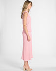Woman standing to the side modeling a light pink pleated shell and skirt on a white backdrop