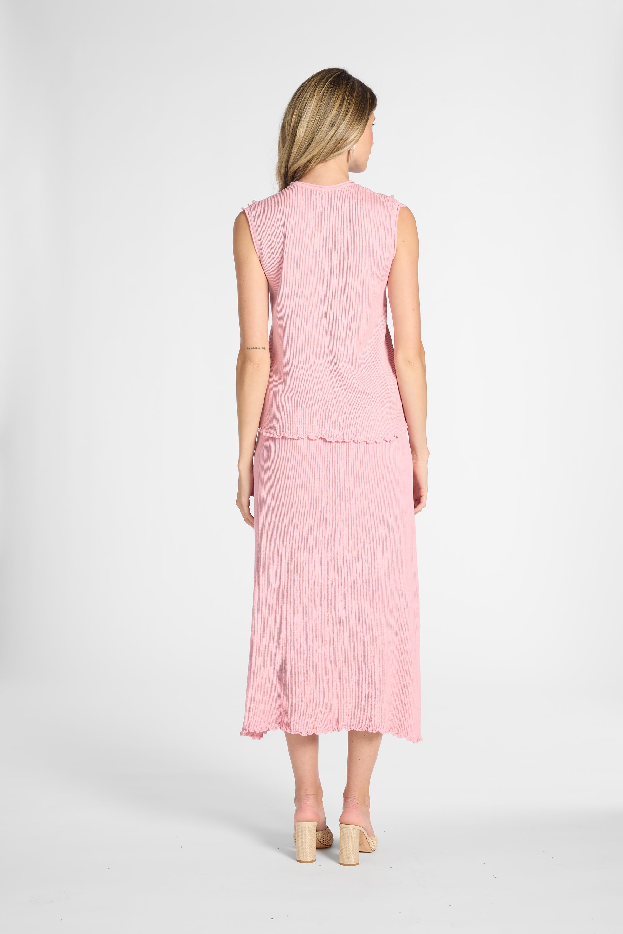 A woman modeling a pink pleated silk skirt and blouse on a white backdrop