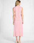 A woman modeling a pink pleated silk skirt and blouse on a white backdrop